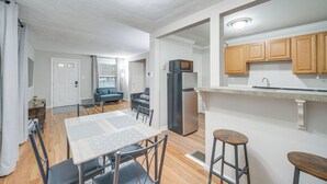 Een moderne keuken met houten kastjes, een roestvrijstalen koelkast, en een eethoek met een tafel en stoelen.