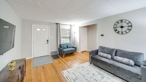 Een woonkamer met een grijze bank, een klok aan de muur en een houten vloer.