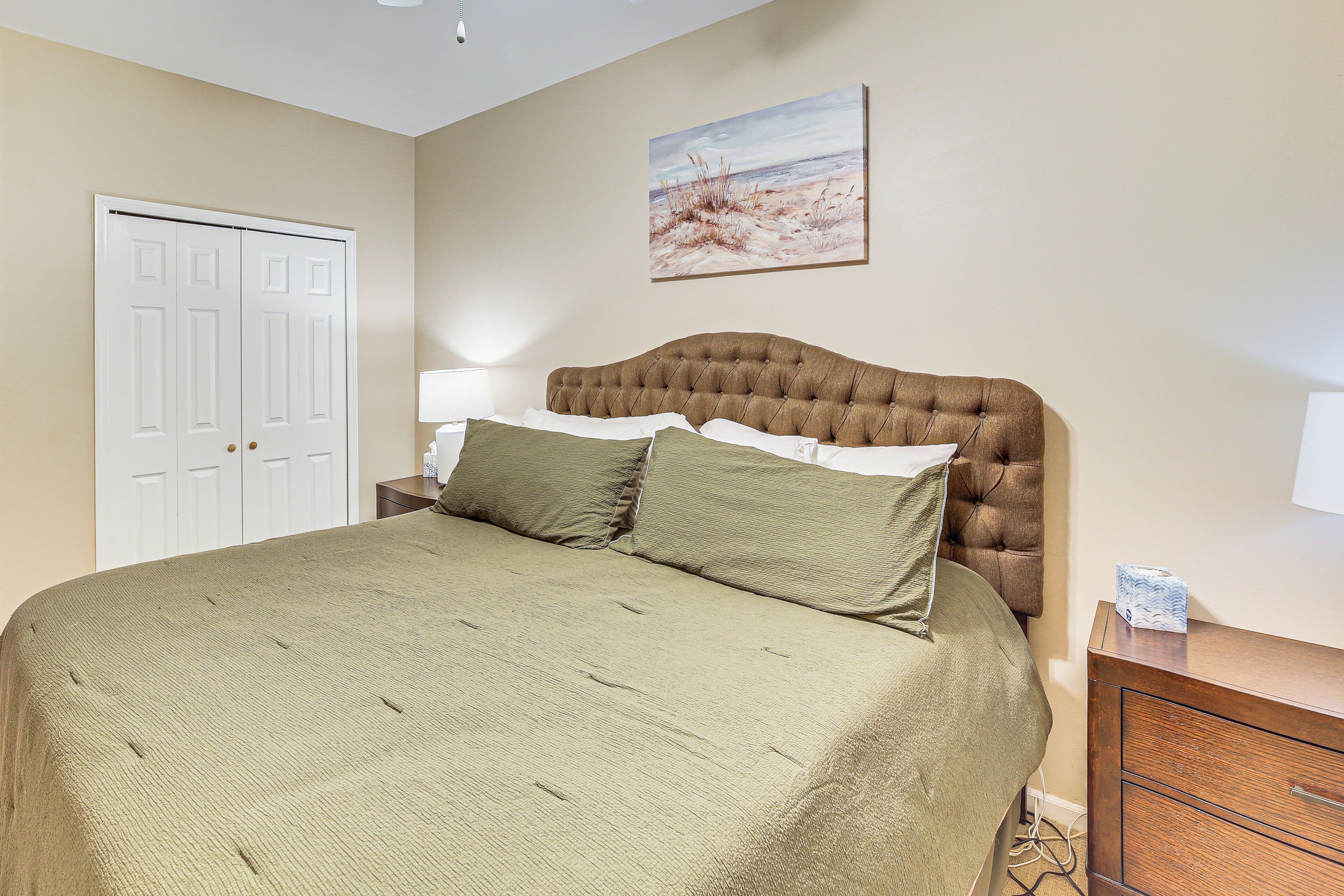 A bedroom with a large bed, a nightstand, a dresser, a door, and a painting on the wall.