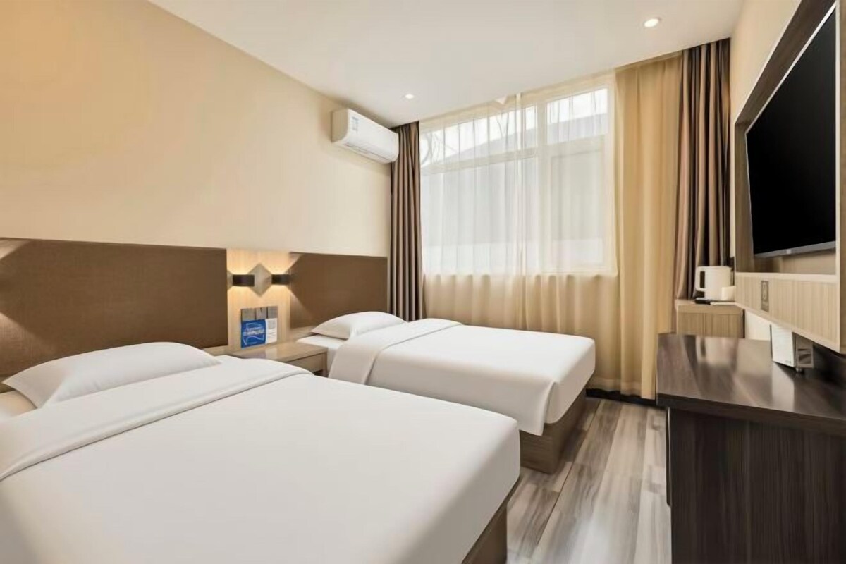 Habitación de hotel con dos camas, un televisor de pantalla plana, un escritorio y una ventana con cortinas.