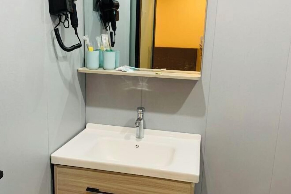 Een badkamer met een witte wastafel, een spiegel, een haardroger en een plank met toiletartikelen.
