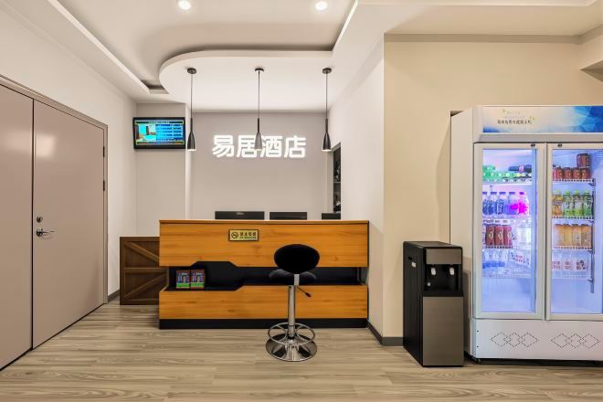 A reception area with a wooden desk, a black chair, a vending machine, and a television on the wall.