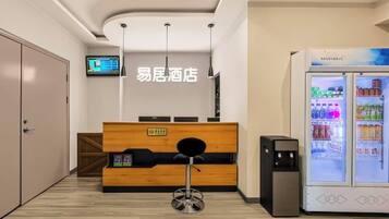 A reception area with a wooden desk, a black chair, a vending machine, and a television on the wall.