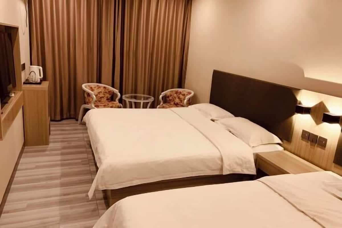 A hotel room with two beds, a desk with a coffee maker, two armchairs, and a small table.