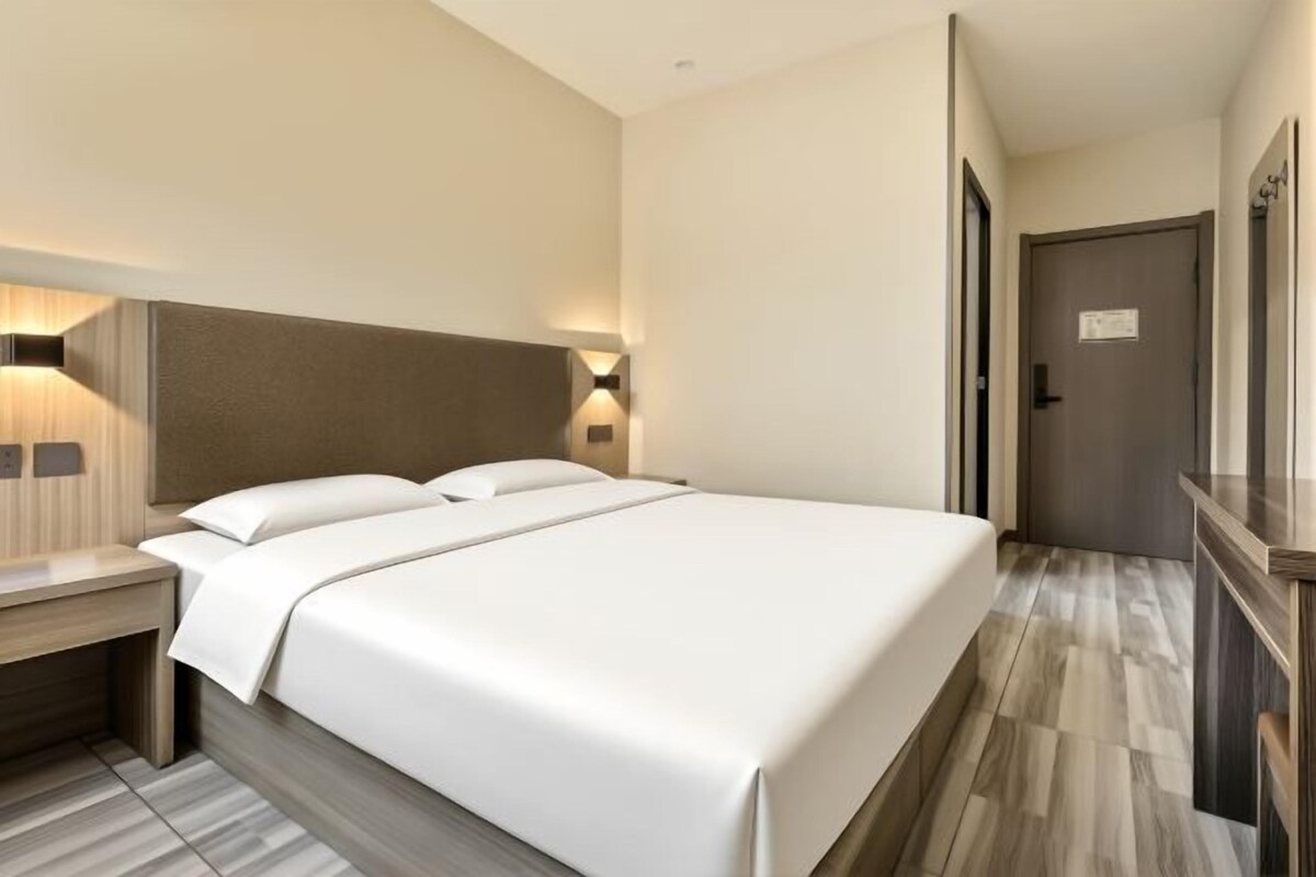 Una habitación de hotel con una cama grande, mesitas de noche y una puerta que da a otra habitación.