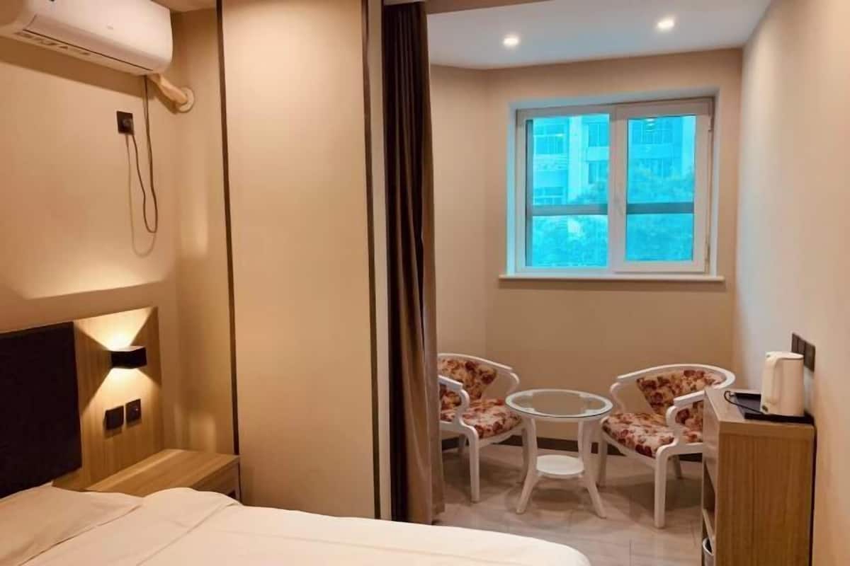 A hotel room with a bed, a desk, two chairs, a window, and a wall-mounted air conditioner.
