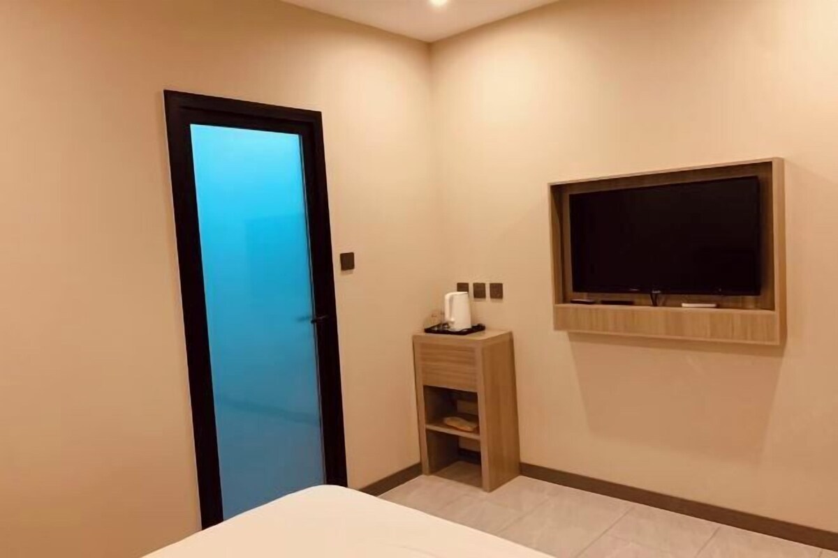 Hotelkamer met een bed, een aan de muur bevestigde televisie, een klein houten kastje en een deur met ruitverdeling.