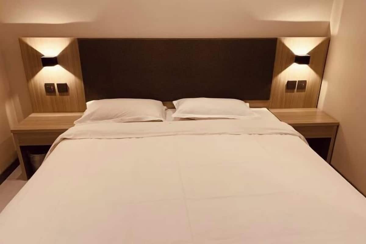 A double bed with a wooden headboard, two bedside tables with wall-mounted lamps, and a neutral color scheme.
