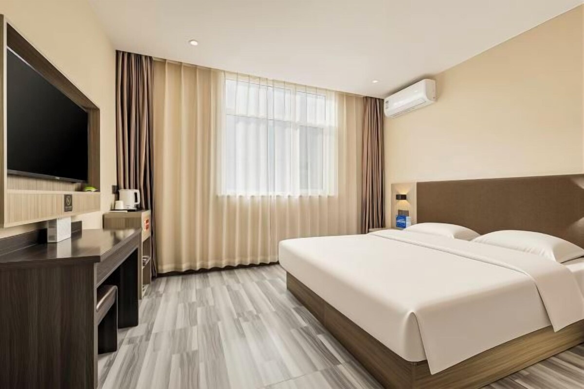 Una habitación de hotel con cama, escritorio, televisor y ventana con cortinas.