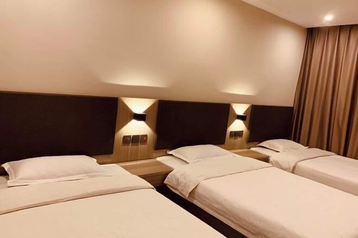 A hotel room with four single beds arranged in a row, each with a wooden nightstand and a wall-mounted lamp.
