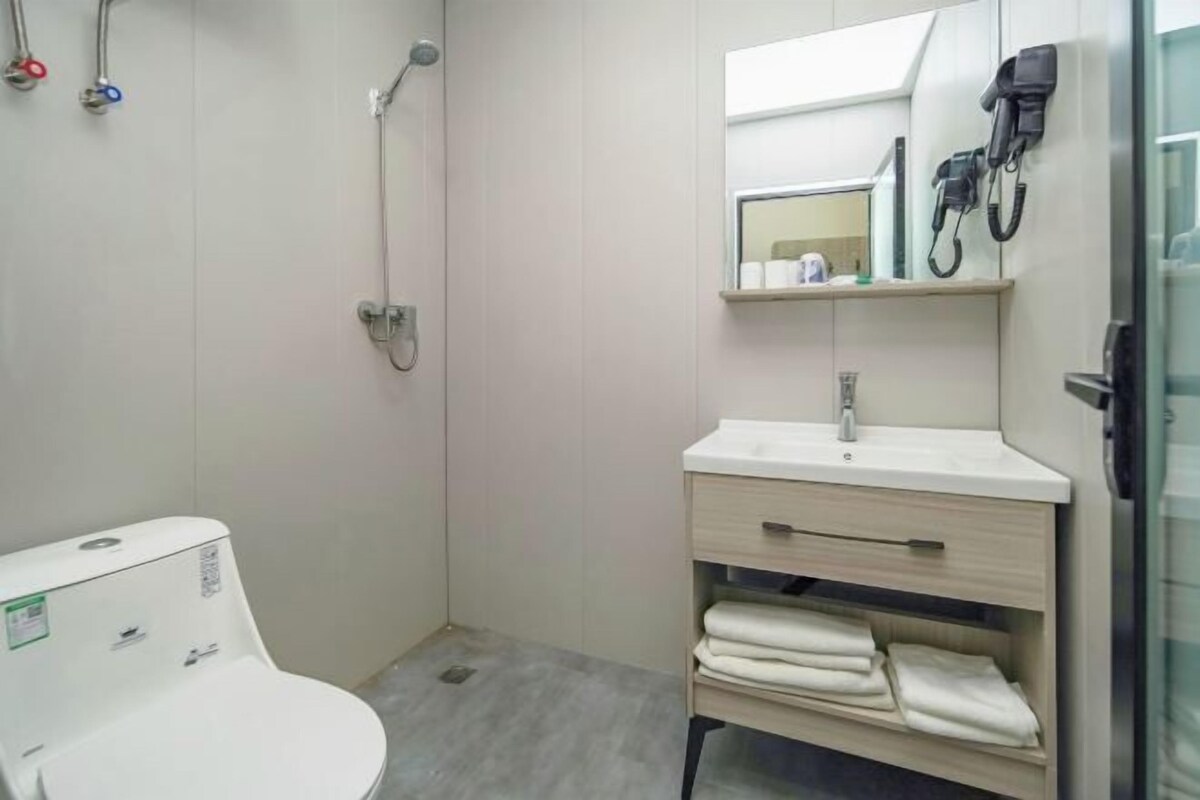 Een moderne badkamer met toilet, douche, wastafel met spiegel en een handdoekrek.