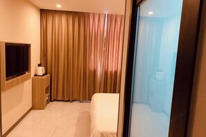 Une chambre d’hôtel dotée d’une grande fenêtre, d’un téléviseur à écran plat fixé au mur, d’une table de chevet avec une lampe et d’une chaise.