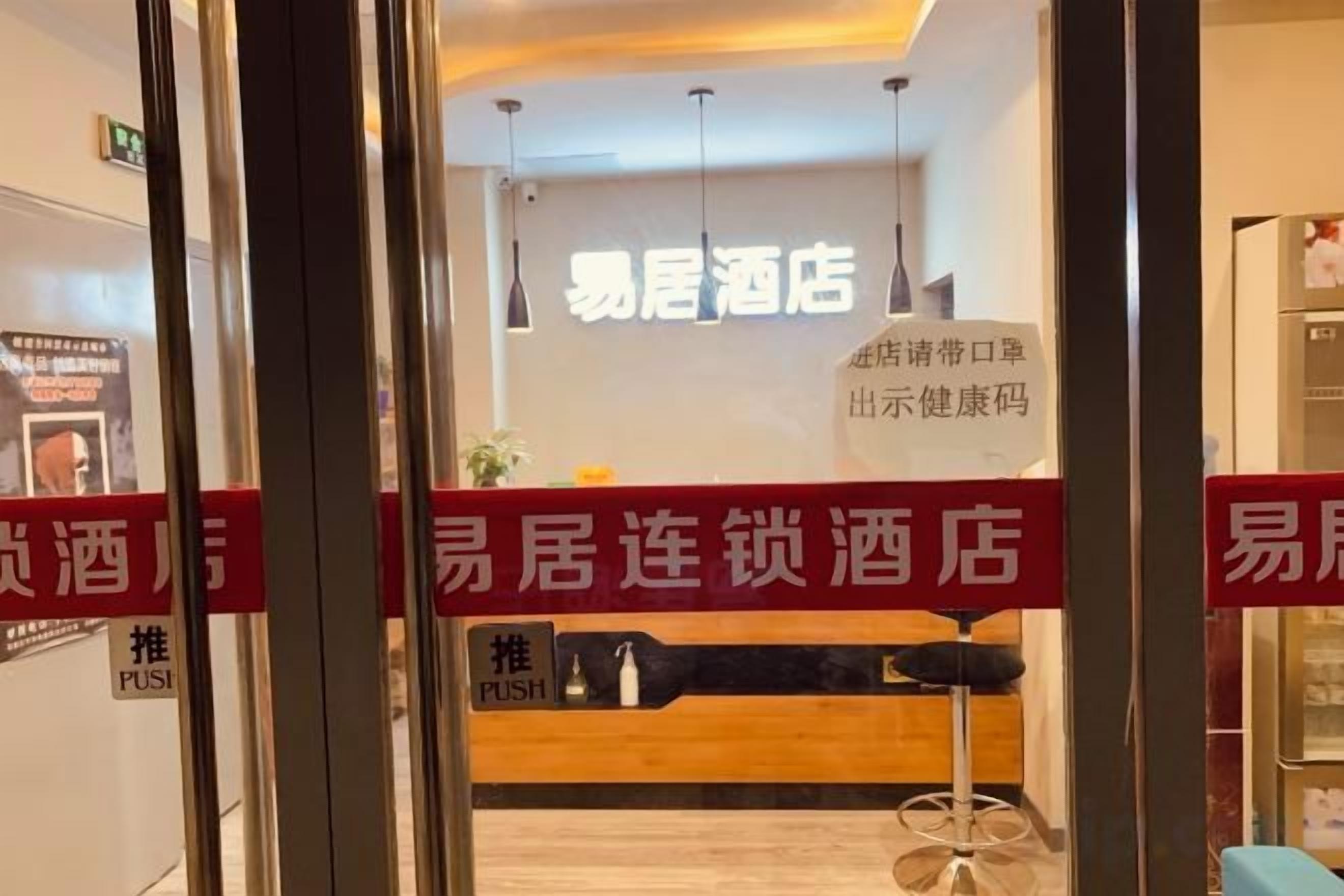 A hotel reception area with a wooden reception desk, a red barrier with white text, and a sign above the desk.