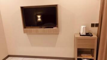 A hotel room with a mounted TV, a bedside table with a lamp, and a trash bin.