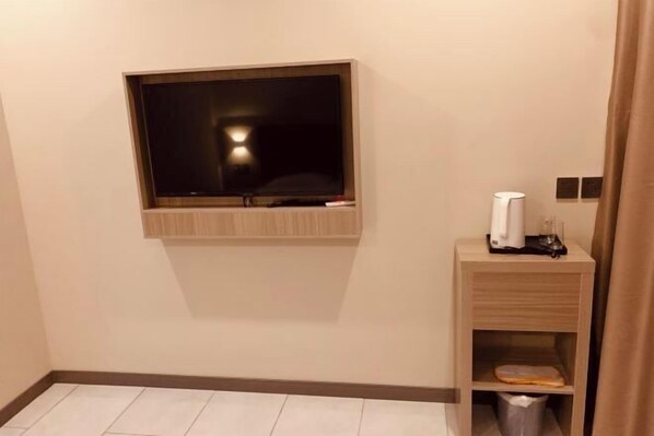 Une chambre d’hôtel équipée d’un téléviseur fixé au mur, d’une table de chevet avec une lampe et d’une poubelle.