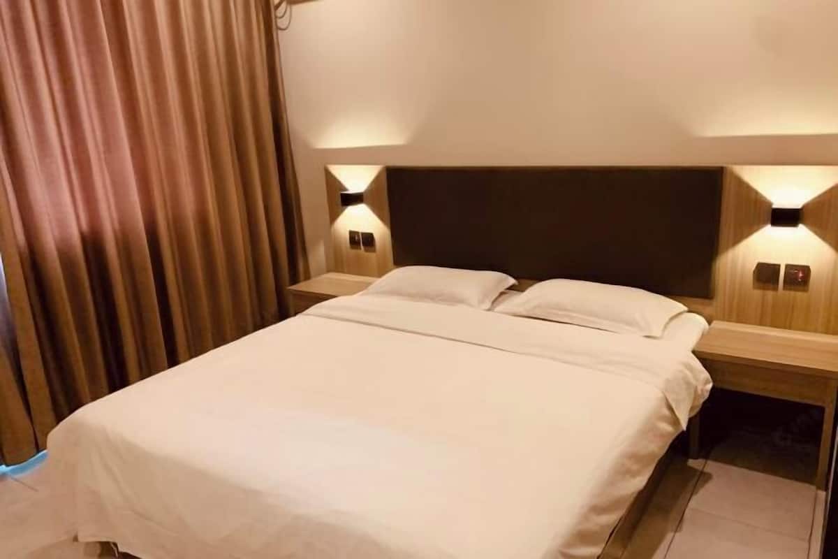 A hotel room with a bed, two bedside tables, and wall-mounted lamps.