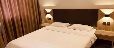 A hotel room with a bed, two bedside tables, and wall-mounted lamps.