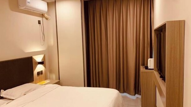 Une chambre d’hôtel avec un lit, une télévision, un minibar et un rideau.