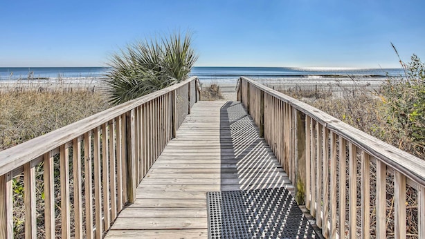 Una passerella di legno che conduce a una spiaggia sotto un cielo sereno.