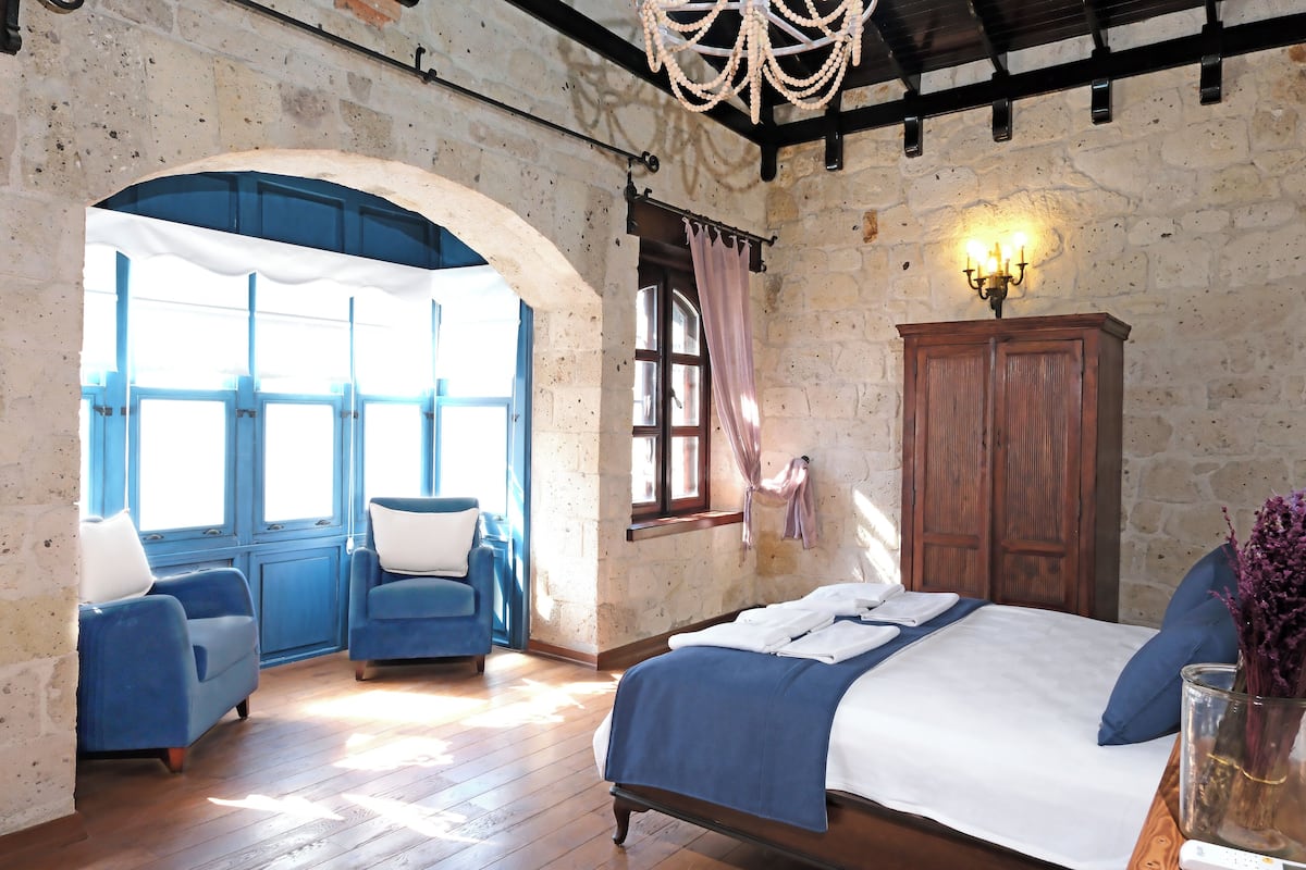 A bedroom with a large bed, two blue armchairs, a wooden wardrobe, and a chandelier.
