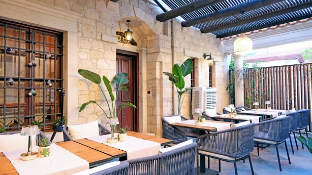 Un espace extérieur aménagé pour les repas, avec des meubles en osier, des murs en pierre et des plantes en pot.