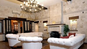 Un salon spacieux avec une cheminée, des canapés en cuir blanc et un lustre.