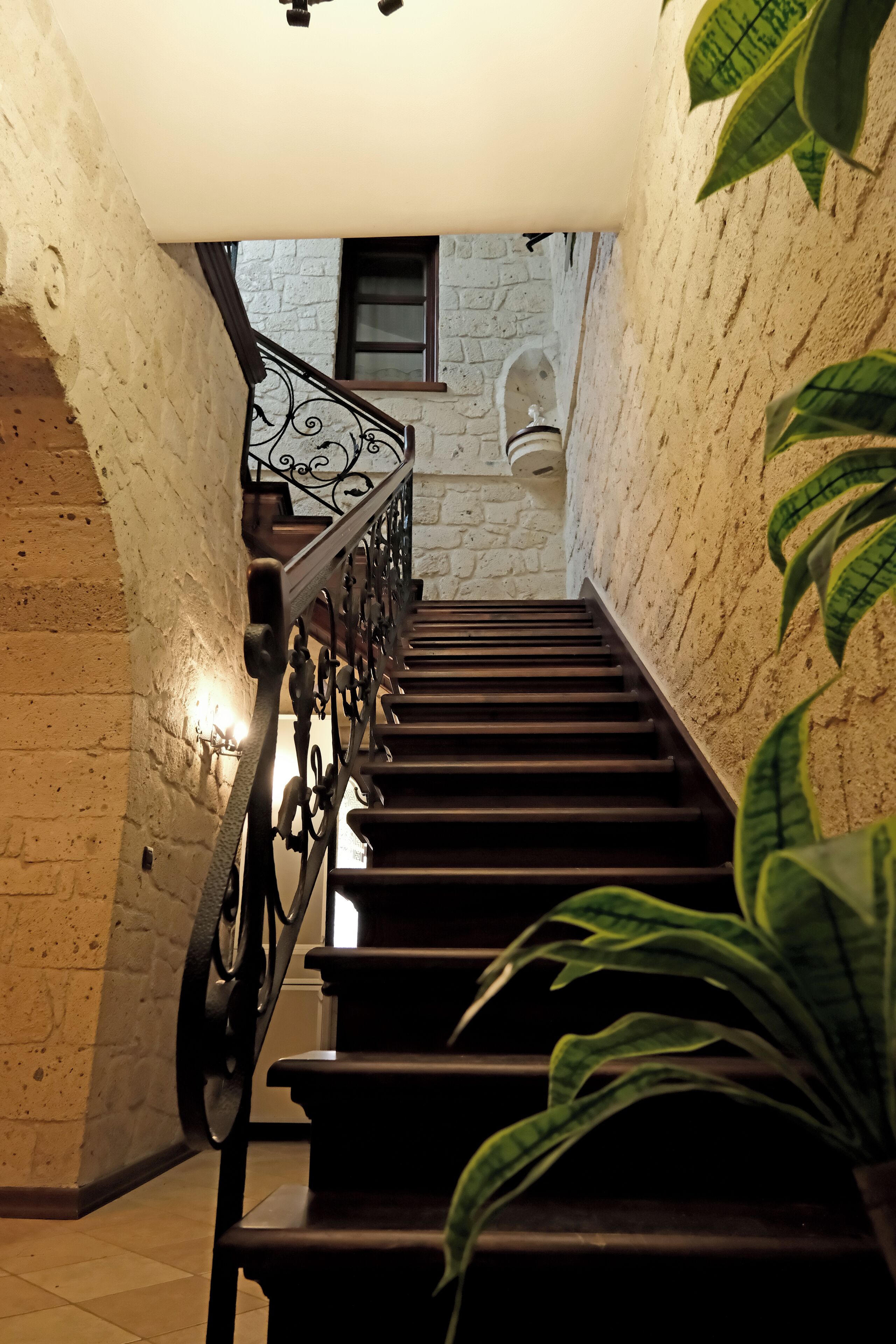 A staircase with a metal railing, flanked by textured walls and a potted plant.
