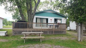 Una cabaña rústica con un porche de madera, una mesa de picnic y un brasero.