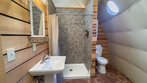 Een badkamer met een houten wastafelmeubel, een witte wasbak, een douchecabine en een toilet.