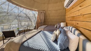Een gezellige, tentachtige kamer met twee bedden, een houten wand en een groot raam met uitzicht op de natuur.