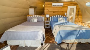 Een knus verblijf in een tent met twee bedden, een houten hoofdbord, een klein nachtkastje met een lamp en een spiegel.