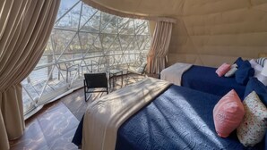 Een gezellig interieur met twee bedden, een kleine tafel en een stoel. Grote ramen bieden uitzicht op de omgeving.