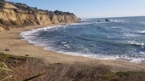 A coastal beach with a sandy shore, waves, and rocky outcrops.