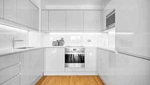 Une cuisine moderne avec des meubles blancs, un four en acier inoxydable et un plancher en bois.