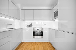 Une cuisine moderne avec des meubles blancs, un four en acier inoxydable et un plancher en bois.