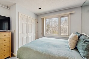 Relax in this serene bedroom with a large window, a comfortable bed, and a flat-screen TV.