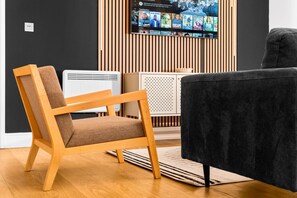 Ein modernes Wohnzimmer mit einem Holzstuhl, einem schwarzen Sofa und einem Flachbildfernseher, der an einer Wand aus Holzpaneelen befestigt ist.