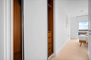 A bedroom with a large window, a bed, and a wooden wardrobe.