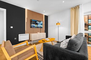 Ein modernes Wohnzimmer mit schwarzer Akzentwand, einem Wand-Fernseher, einer Couch, einem Couchtisch und einer Stehlampe.