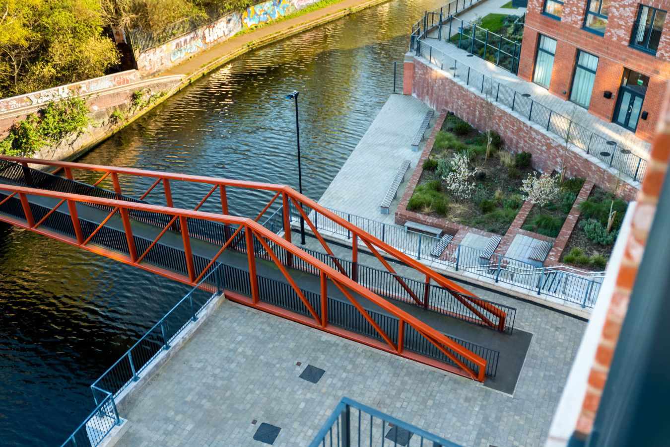 Un puente rojo sobre un río, con un edificio y vegetación al fondo.