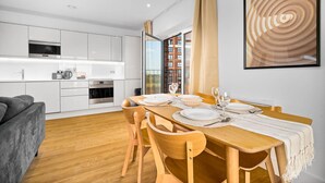 Una cocina moderna con armarios blancos, horno empotrado y comedor con una mesa de madera para cuatro comensales.