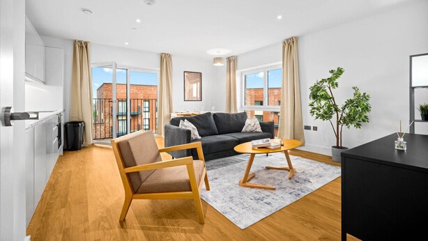 Una sala de estar moderna con un sofá, sillones y una mesa de centro. Se ve un edificio de ladrillo a través de grandes ventanales.