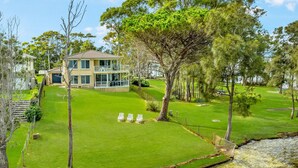 Un bâtiment à deux étages doté d’un balcon, entouré d’une pelouse bien entretenue et d’arbres.