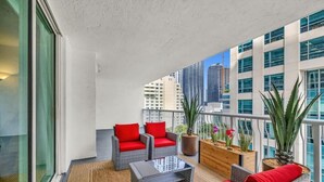 A balcony with wicker furniture, red cushions, and potted plants.