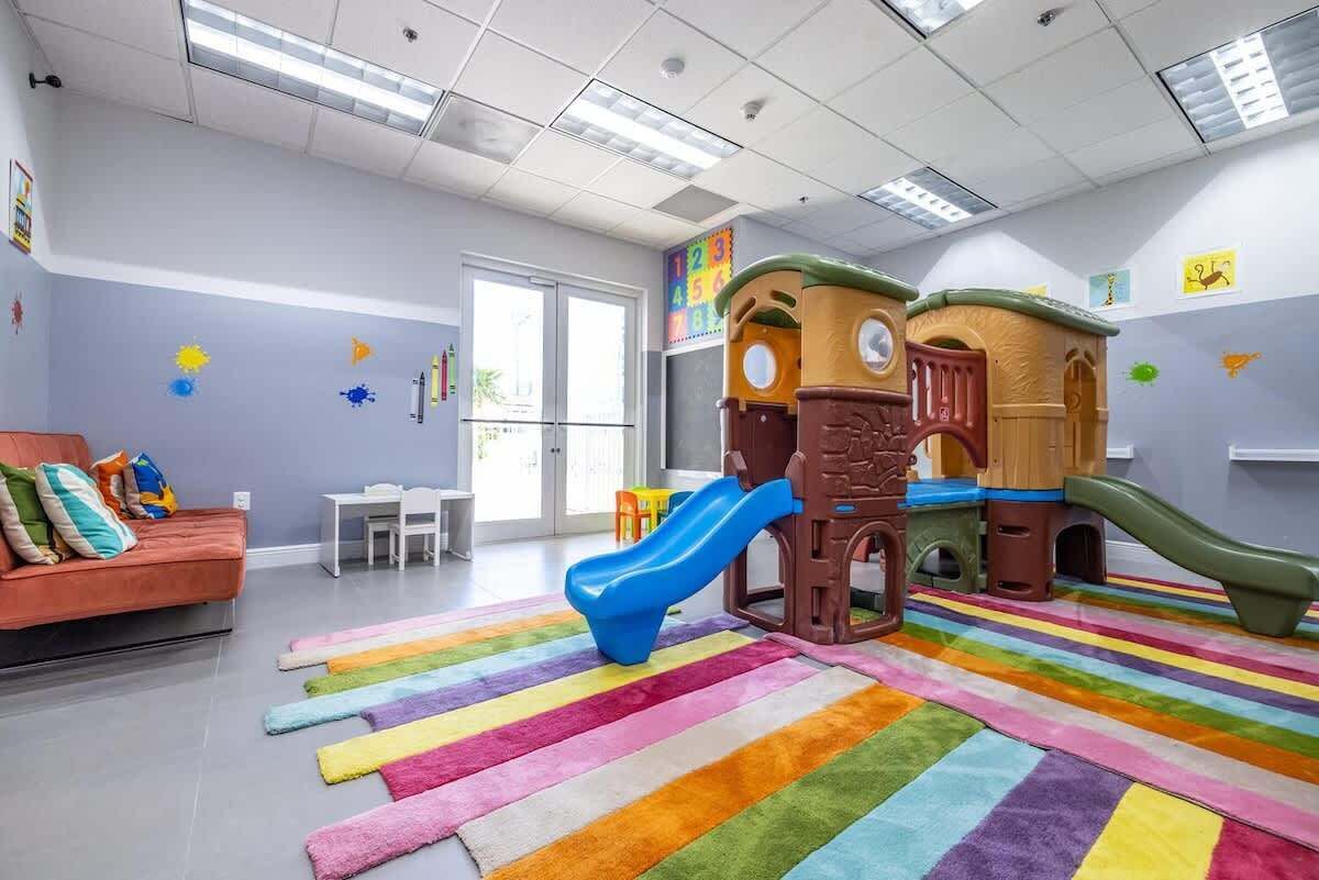 A children's play area with a slide, play structures, and a colorful striped rug.