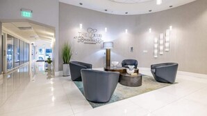 A modern lobby with a reception desk, grey sofas, a coffee table, and a wall sign reading "The Club at Brickell Bay".