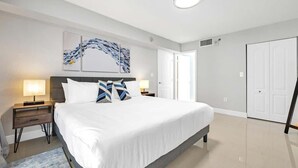 A modern bedroom with a large bed, two bedside tables with lamps, a ceiling light, and a door.