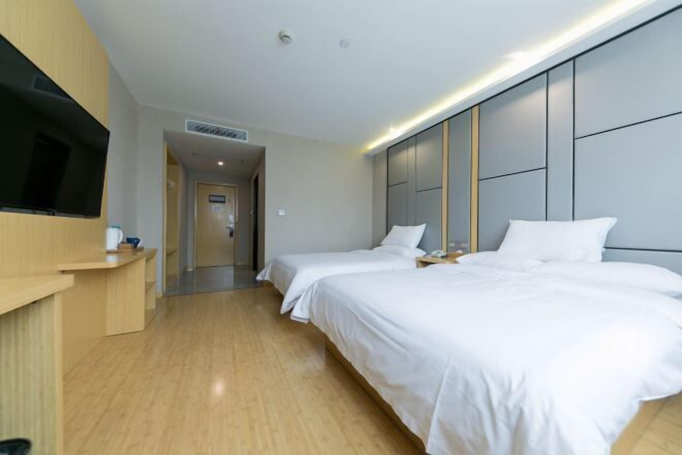 A modern hotel room with two single beds, a flat-screen TV mounted on the wall, and a wooden floor.
