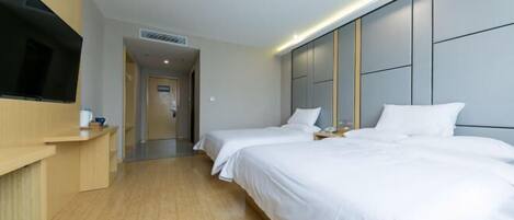 A modern hotel room with two single beds, a flat-screen TV mounted on the wall, and a wooden floor.