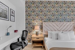 Ein Hotelzimmer mit einem Bett, einem Schreibtisch, einem Stuhl, einem Nachttisch mit Lampe und einer Wand mit Muster.